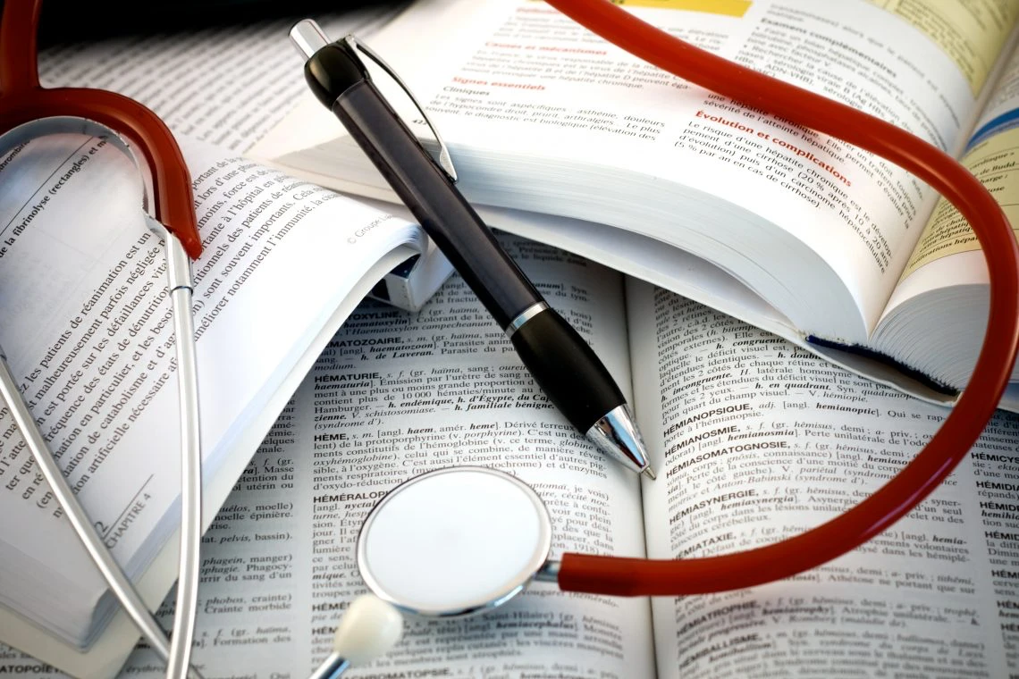 Stéthoscope, livres médicaux et stylo sur table.