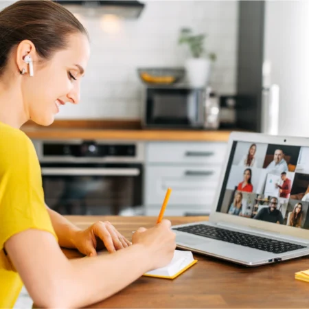 Femme note durant une visioconférence sur ordinateur portable.