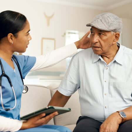 elderly care, nurse and senior man on sofa for consultation, routine check up and diagnosis in living room. female carer, retired patient and assessment on couch for healthcare, wellbeing or medicare